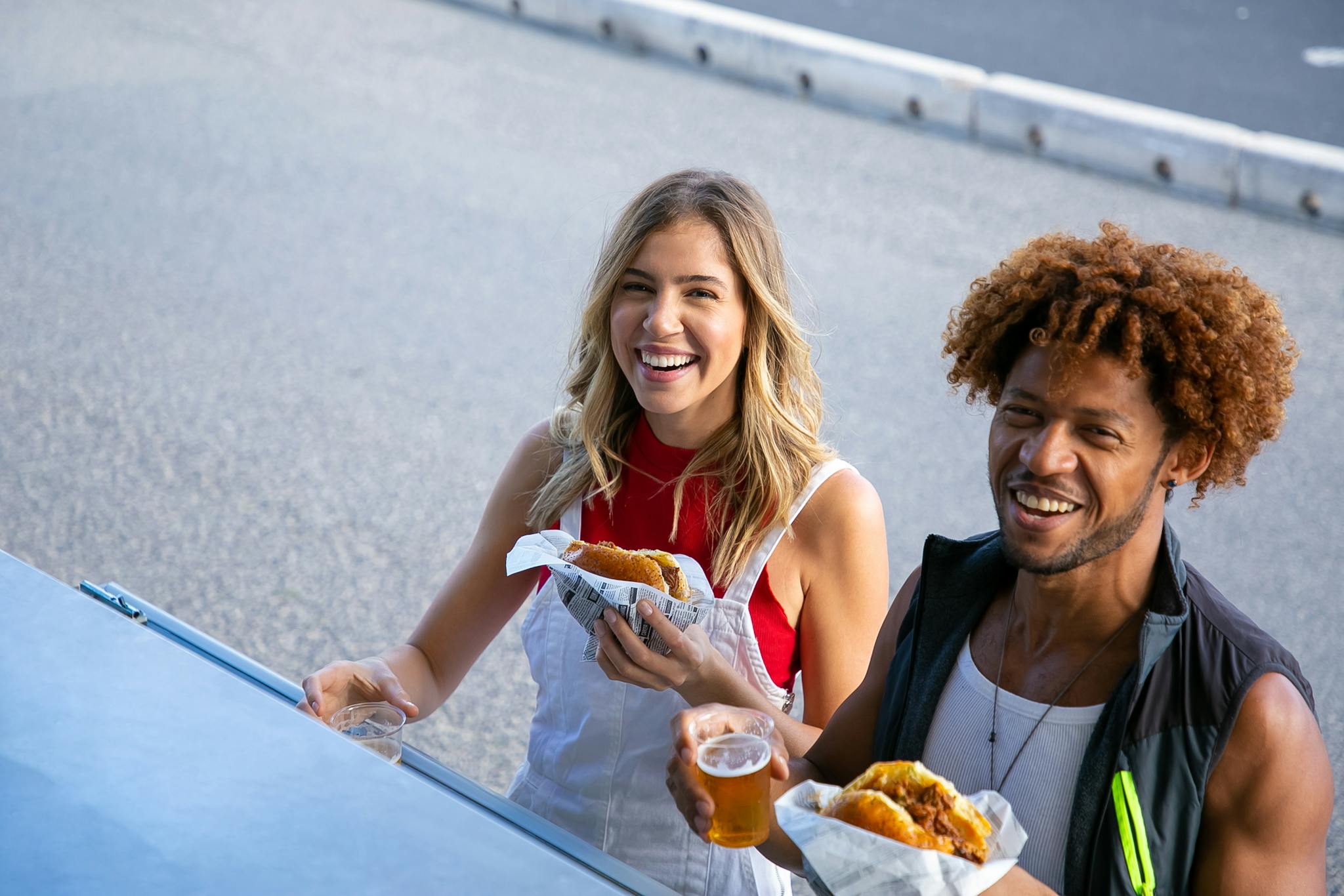 Delighted multiethnic couple with drinks and food on street